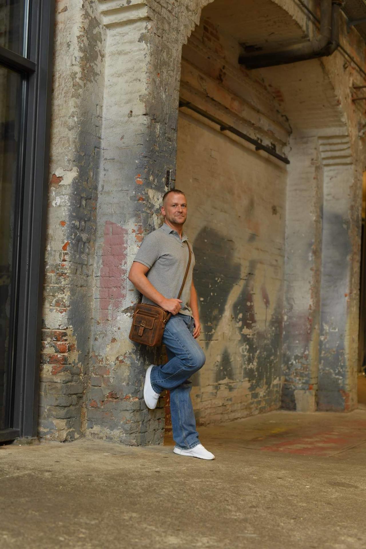 Mann mit Ledertasche im Vintage Look lehnt sich an Mauerwerk an